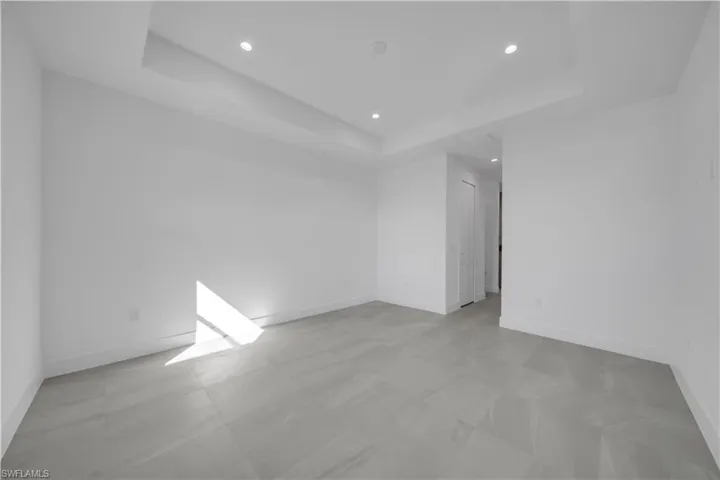 Empty room featuring recessed lighting, a raised ceiling, and light floors
