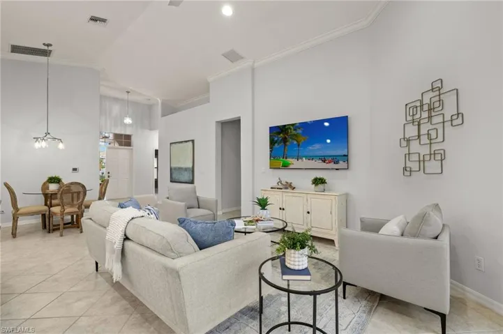 Living room featuring high vaulted ceiling, light tile patterned flooring, crown molding, and a chandelier