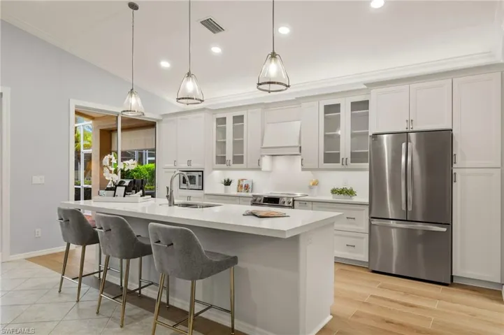 Kitchen with premium range hood, appliances with stainless steel finishes, a kitchen island with sink, white cabinets, and sink