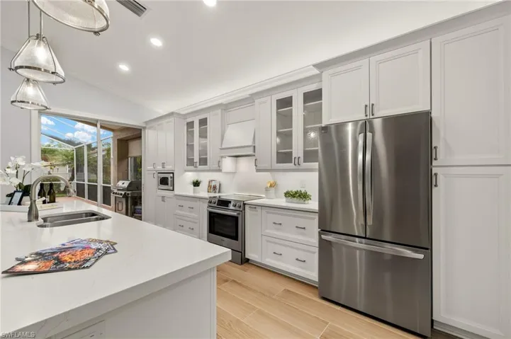 Kitchen featuring custom exhaust hood, stainless steel appliances, hanging light fixtures, white cabinets, and sink