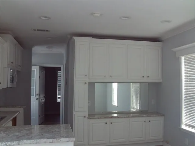 Kitchen featuring ornamental molding, white cabinets, visible vents, and light stone counters
