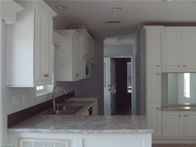 Kitchen featuring light stone counters, a sink, visible vents, white cabinetry, and crown molding