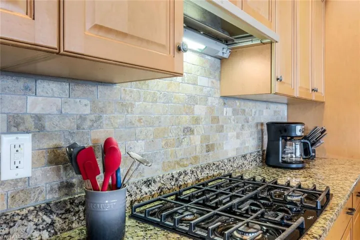Kitchen with light brown cabinets, gas stovetop, and backsplash