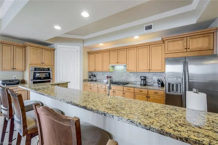 Kitchen featuring tasteful backsplash, stainless steel appliances, light stone counters, a kitchen breakfast bar, and ornamental molding!