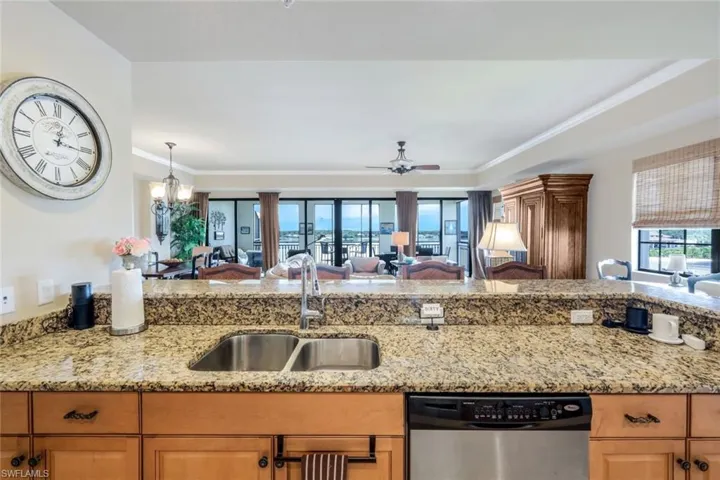 Kitchen with sink, dishwasher, ceiling fan with notable chandelier, and light stone counters