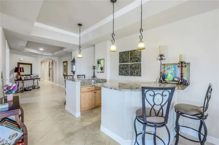 Separate Wet bar area, decorative light fixtures, light tile patterned floors, light stone countertops, and a tray ceiling
