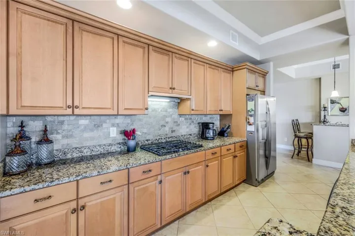 Kitchen featuring tasteful backsplash, a raised ceiling, appliances with stainless steel finishes, stone countertops, and light tile patterned floors!