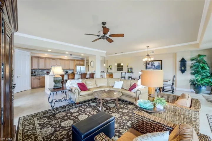 Grand room facing kitchen with ceiling fan with notable chandelier, crown molding, light tile patterned floors, and a tray ceiling