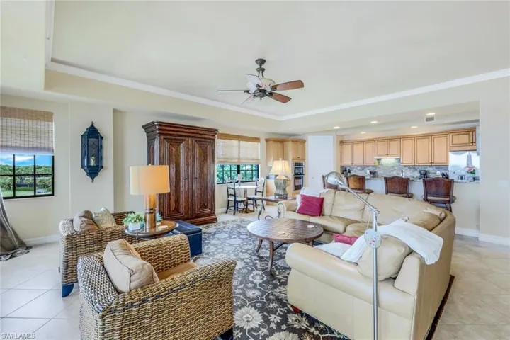Living room featuring light tile patterned flooring, a raised ceiling, crown molding, and ceiling fan