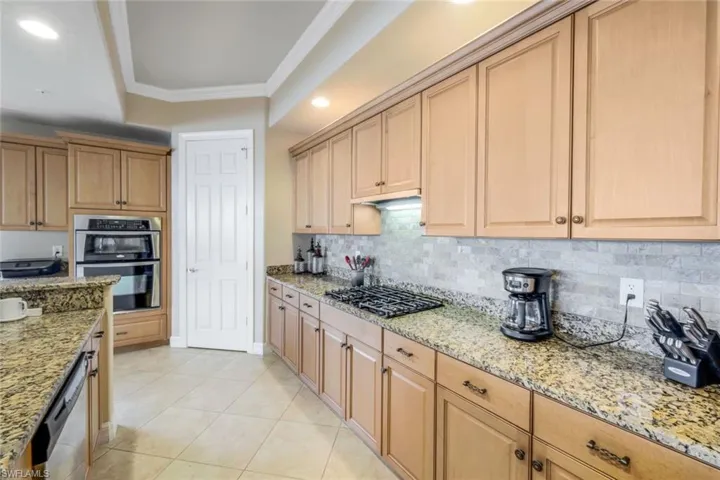 Kitchen with crown molding, light stone counters, appliances with stainless steel finishes, and decorative backsplash