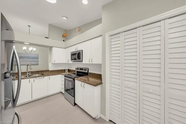 Kitchen featuring appliances with stainless steel finishes, white cabinets, dark stone counters, and a chandelier