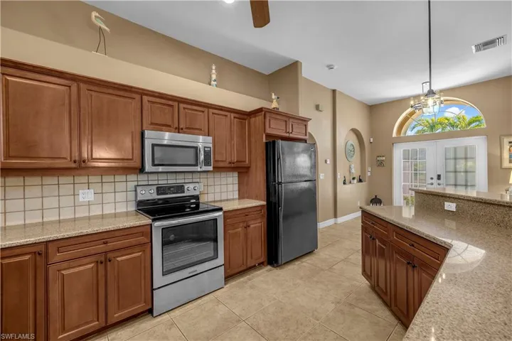 Kitchen with stainless steel appliances, light stone counters, wood finish cabinetry, a ceiling fan, and french doors