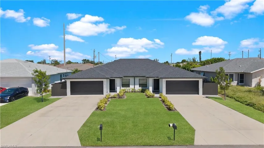 Duplex exterior featuring a dark shingle roof, white exterior walls, dark garage doors, concrete driveways, and manicured landscaping