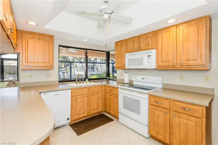 Kitchen with sink, light tile patterned floors, ceiling fan, a tray ceiling, and white appliances