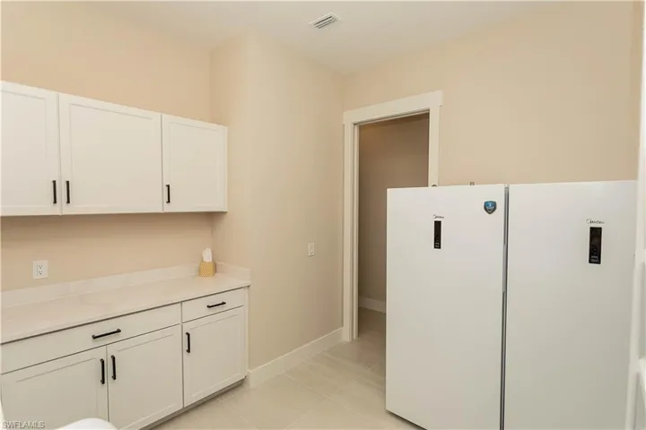 Laundry room has been remodeled with pocket door, extra freestanding refrigerator and freezer conveys, white cabinetry, and light tile patterned floors