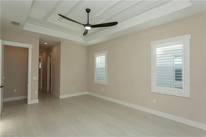 Owner's suite with a ceiling fan, custom glass door privacy screen, plantation shutters, ceiling fan under decorative ceiling.