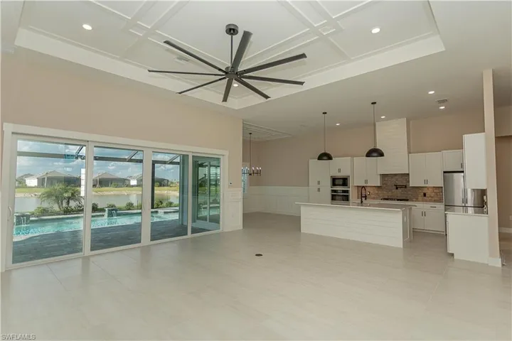 Unfurnished living room, great room, island in kitchen, white cabinets, wainscoted wall, custom fireplace, a decorative ceiling, ceiling fan, recessed lighting, and views of pool/spa