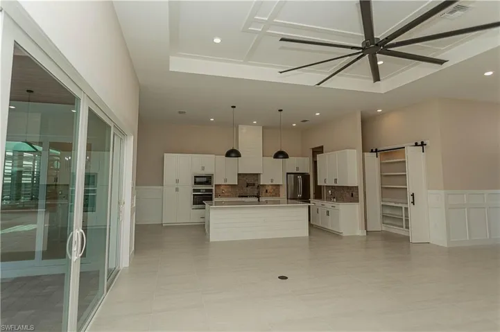 Kitchen with white cabinets, an island with upgraded matte black sink, quartz countertops, pot filler, tile backsplash, upgraded pantry, decorative light fixtures, and stainless steel appliances,  views of pool/spa and golf course lake.