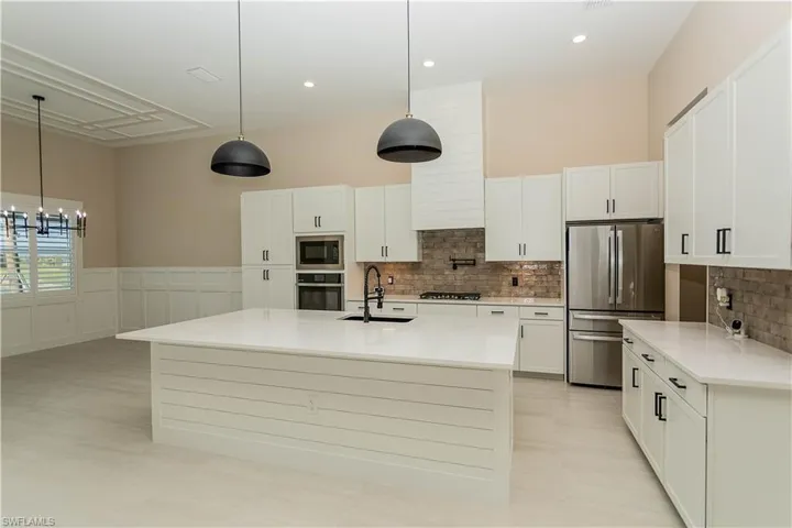 Kitchen with white cabinets, an island with upgraded matte black sink, quartz countertops, pot filler, tile backsplash, upgraded pantry, decorative light fixtures, and stainless steel appliances,  views of pool/spa and golf course lake.