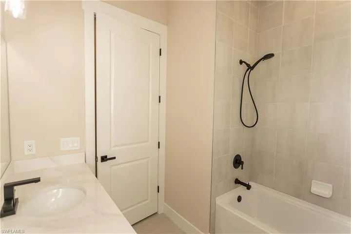 Guest bath featuring vanity and shower / tub combination, floor to ceiling upgraded shower tile, upgraded matte black fixtures, upgraded plantation shutters
