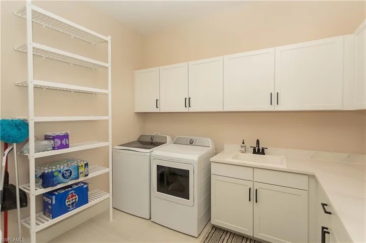 Laundry room has been remodeled with pocket door, extra freestanding refrigerator and freezer conveys, white cabinetry, and light tile patterned floors