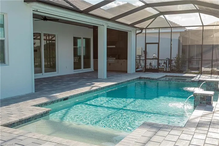 Salt water gas heated concrete pool / spa under screened lanai with sealed pavers and custom outdoor kitchen, views of lake/golf course