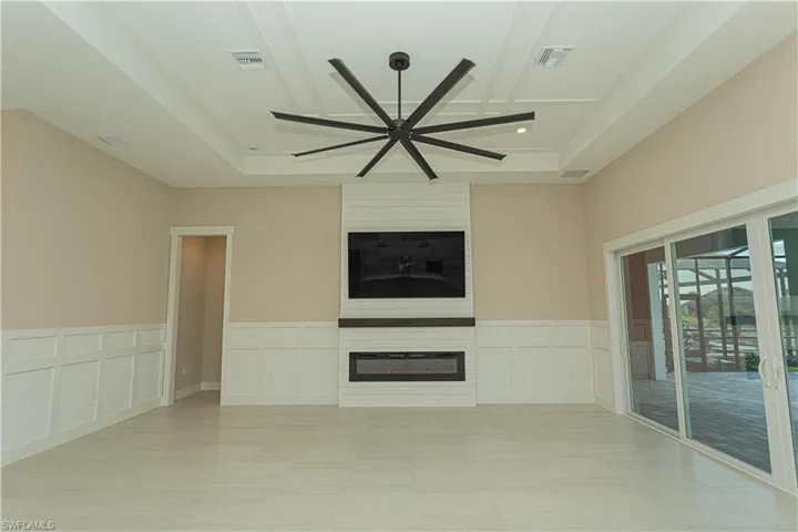 Unfurnished living room with ceiling fan, a fireplace, a decorative wall, light tile patterned flooring, and a wainscoted wall, upgraded fire place