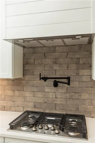 Kitchen view of stainless steel gas stovetop, pot filler, white cabinetry, and decorative tile backsplash
