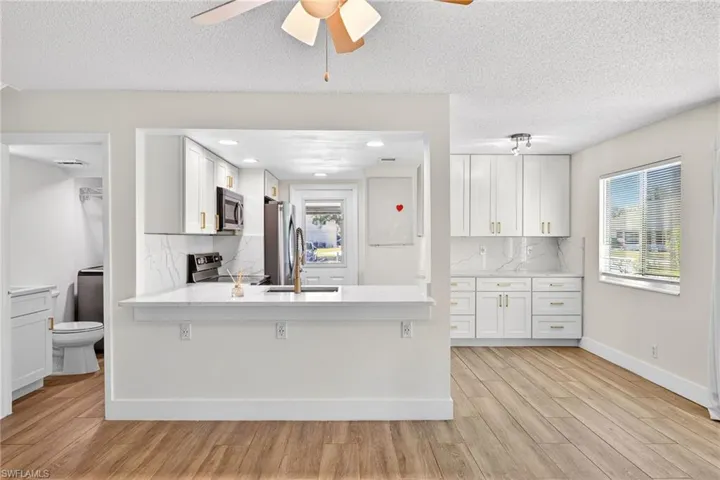 Kitchen featuring decorative backsplash, a textured ceiling, white cabinetry, light wood finished floors, and appliances with stainless steel finishes