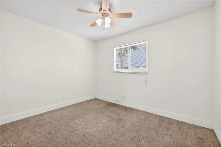 Carpeted empty room with a textured ceiling and a ceiling fan
