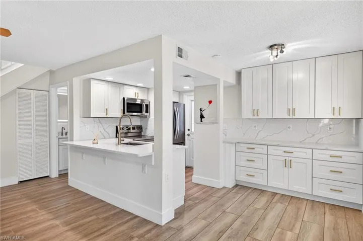 Kitchen with decorative backsplash, white cabinets, light stone countertops, appliances with stainless steel finishes, and a textured ceiling