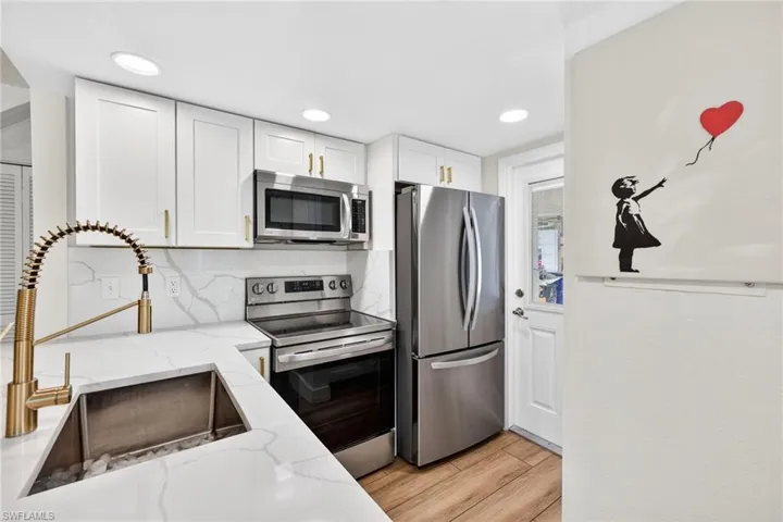 Kitchen with stainless steel appliances, white cabinets, light stone countertops, tasteful backsplash, and recessed lighting