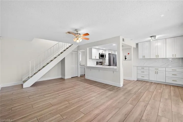 Unfurnished living room with a textured ceiling, a ceiling fan, light wood-style floors, and stairway