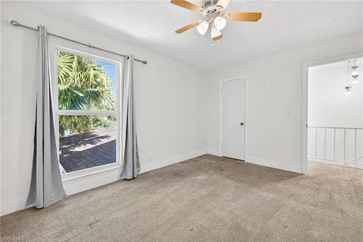 Empty room with light carpet, a textured ceiling, and a ceiling fan