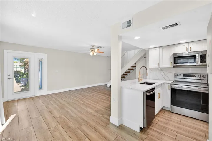 Kitchen featuring appliances with stainless steel finishes, open floor plan, white cabinetry, light stone countertops, and light wood finished floors