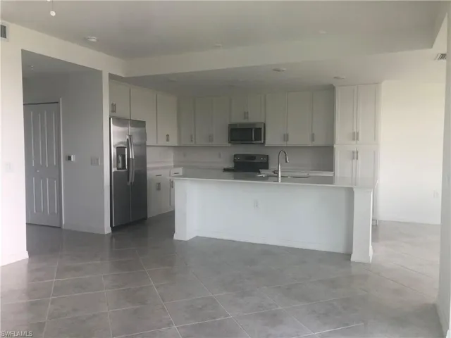Kitchen with a center island with sink, light tile flooring, sink, and appliances with stainless steel finishes
