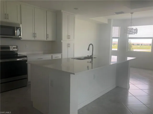 Kitchen with decorative light fixtures, a kitchen island with sink, white cabinetry, appliances with stainless steel finishes, and sink