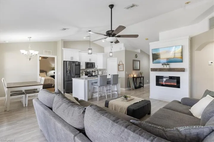 Living room featuring vaulted ceiling, ceiling fan with notable chandelier, and light hardwood / wood-style flooring