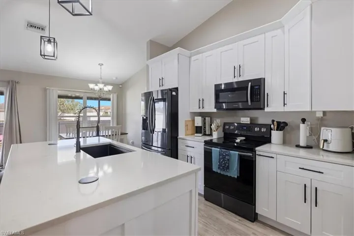 Kitchen with sink, refrigerator with ice dispenser, black range with electric stovetop, hanging light fixtures, and white cabinets