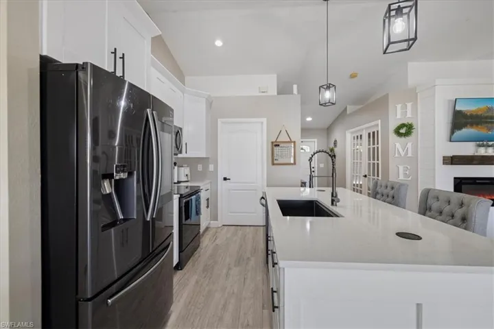 Kitchen with stainless steel refrigerator with ice dispenser, lofted ceiling, sink, pendant lighting, and white cabinets