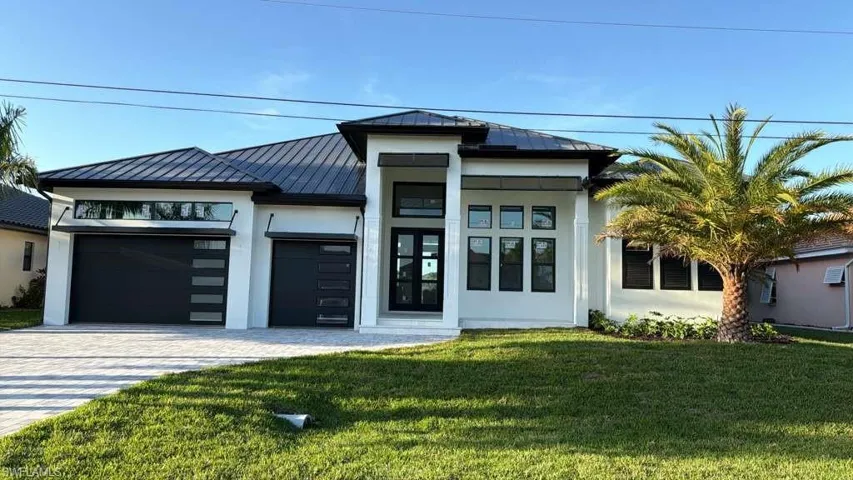 View of front of property featuring a standing seam roof, an attached garage, a front lawn, and decorative driveway