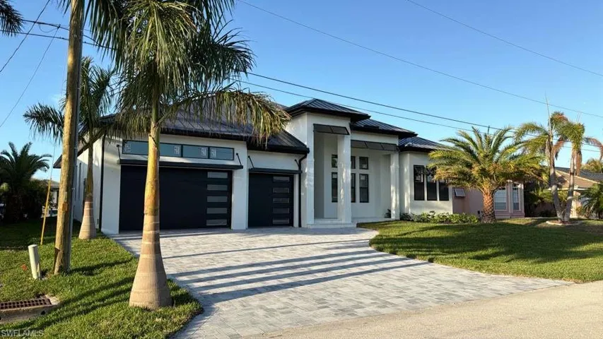 View of front of home featuring decorative driveway, an attached garage, a standing seam roof, a front lawn, and stucco siding