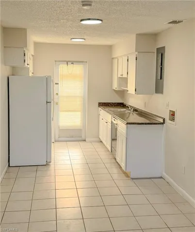 Kitchen with freestanding refrigerator, dark countertops, white cabinets, light tile patterned floors, and a textured ceiling