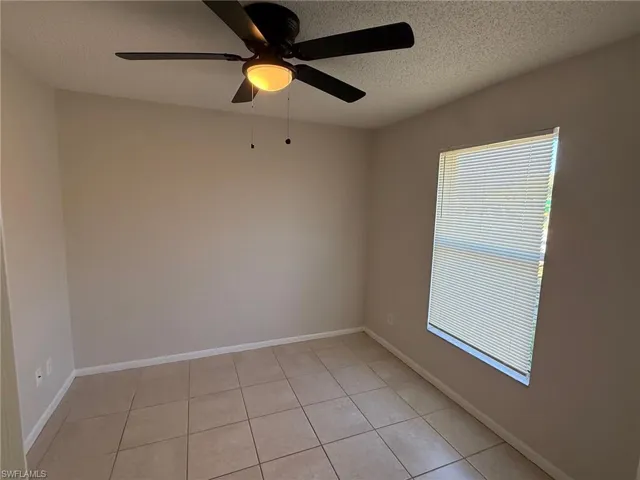 Empty room with a textured ceiling, a ceiling fan, and light tile patterned flooring