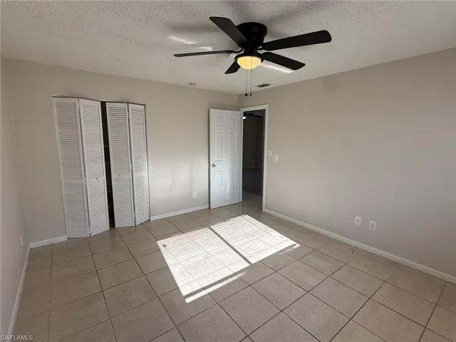 Unfurnished bedroom featuring a closet, a textured ceiling, a ceiling fan, and light tile patterned floors