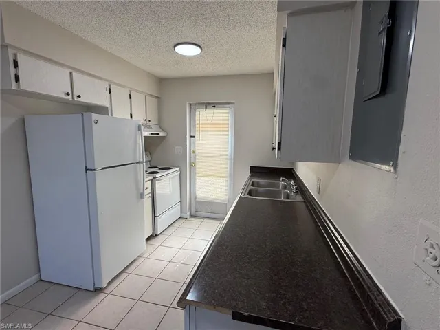 Kitchen with white appliances, a textured ceiling, dark countertops, white cabinetry, and light tile patterned floors