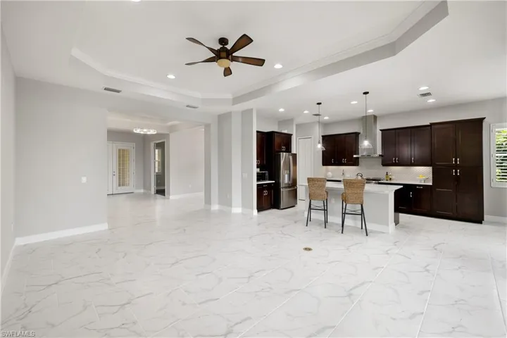 Kitchen featuring wall chimney range hood, a tray ceiling, a center island, stainless steel fridge, and a breakfast bar