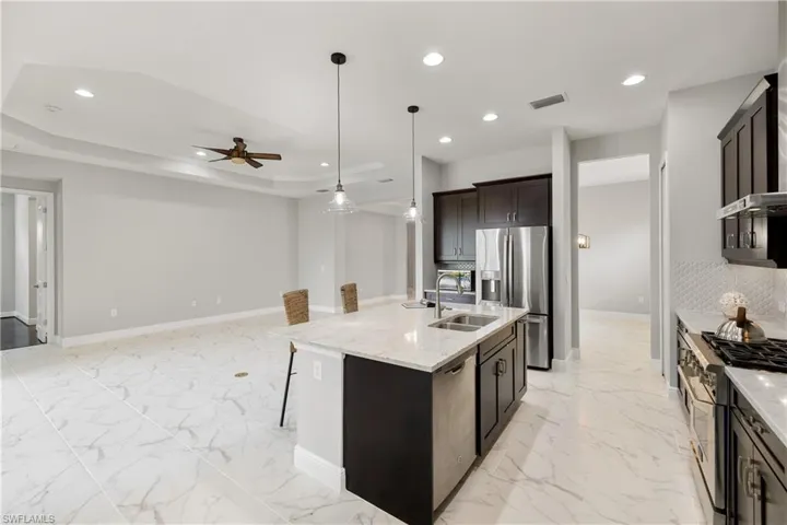 Kitchen with an island with sink, ceiling fan, light stone countertops, appliances with stainless steel finishes, and sink