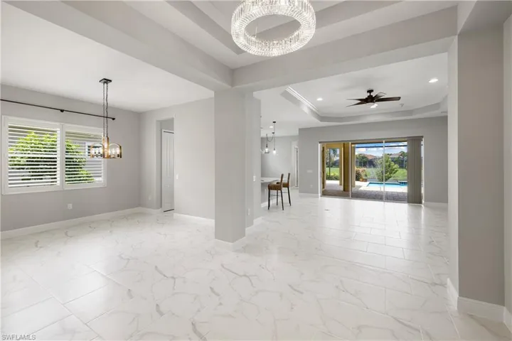 Tiled spare room with ceiling fan with notable chandelier and a raised ceiling