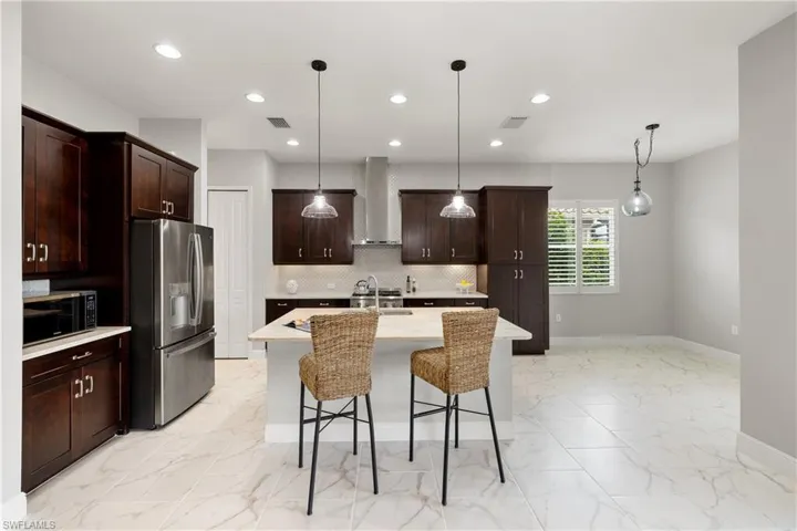 Kitchen with stainless steel appliances, wall chimney exhaust hood, decorative backsplash, pendant lighting, and a center island with sink